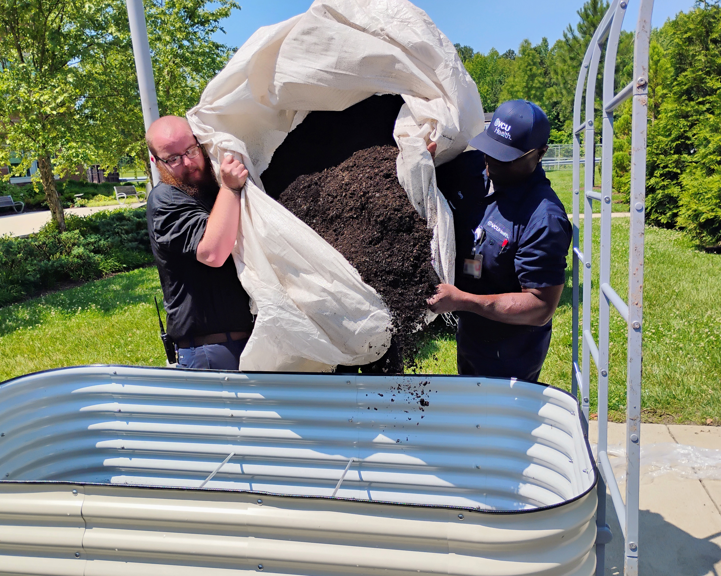 two men dumping a large bag of mulch into a raised garden bed