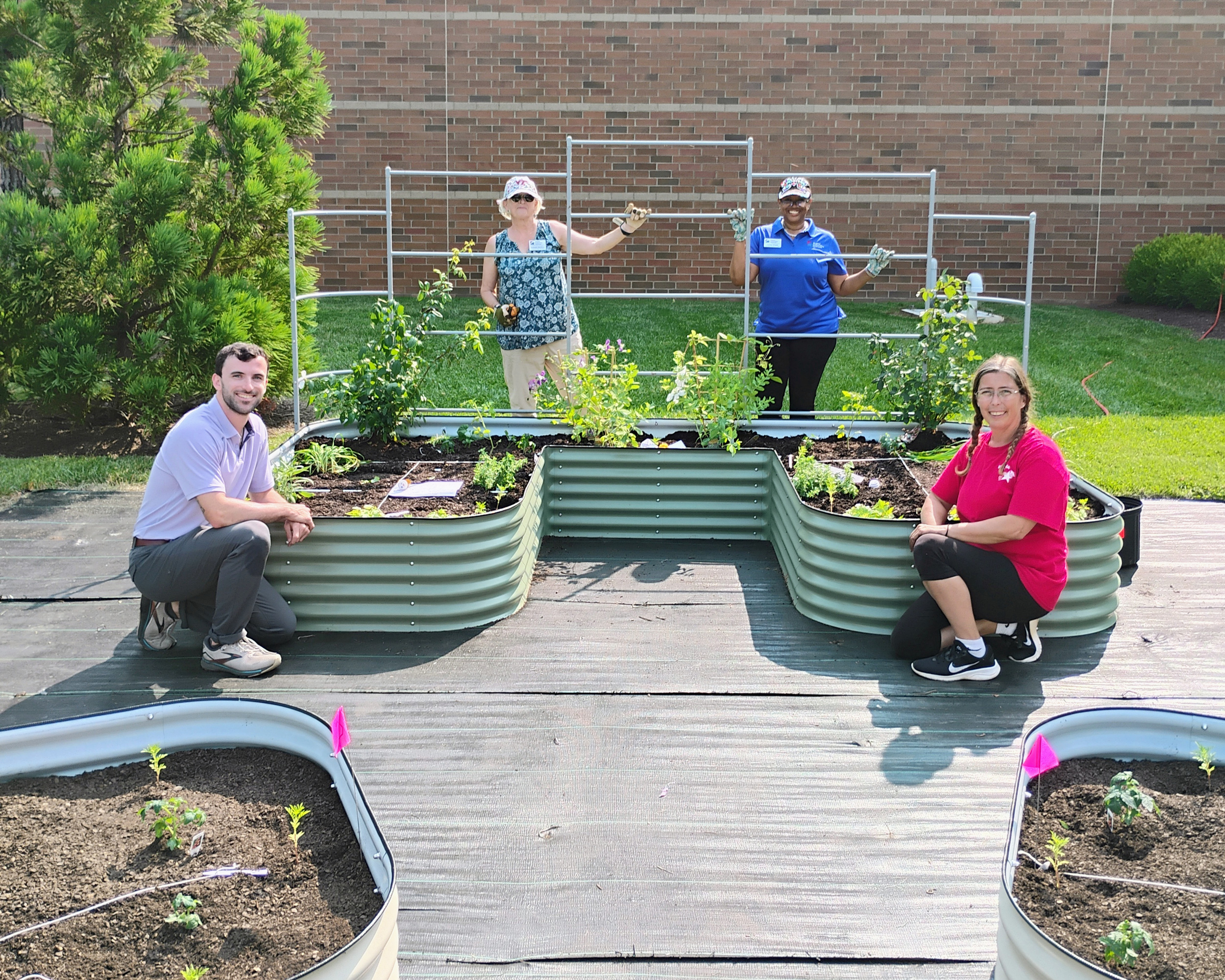 people smiling while standing with a raised garden bed